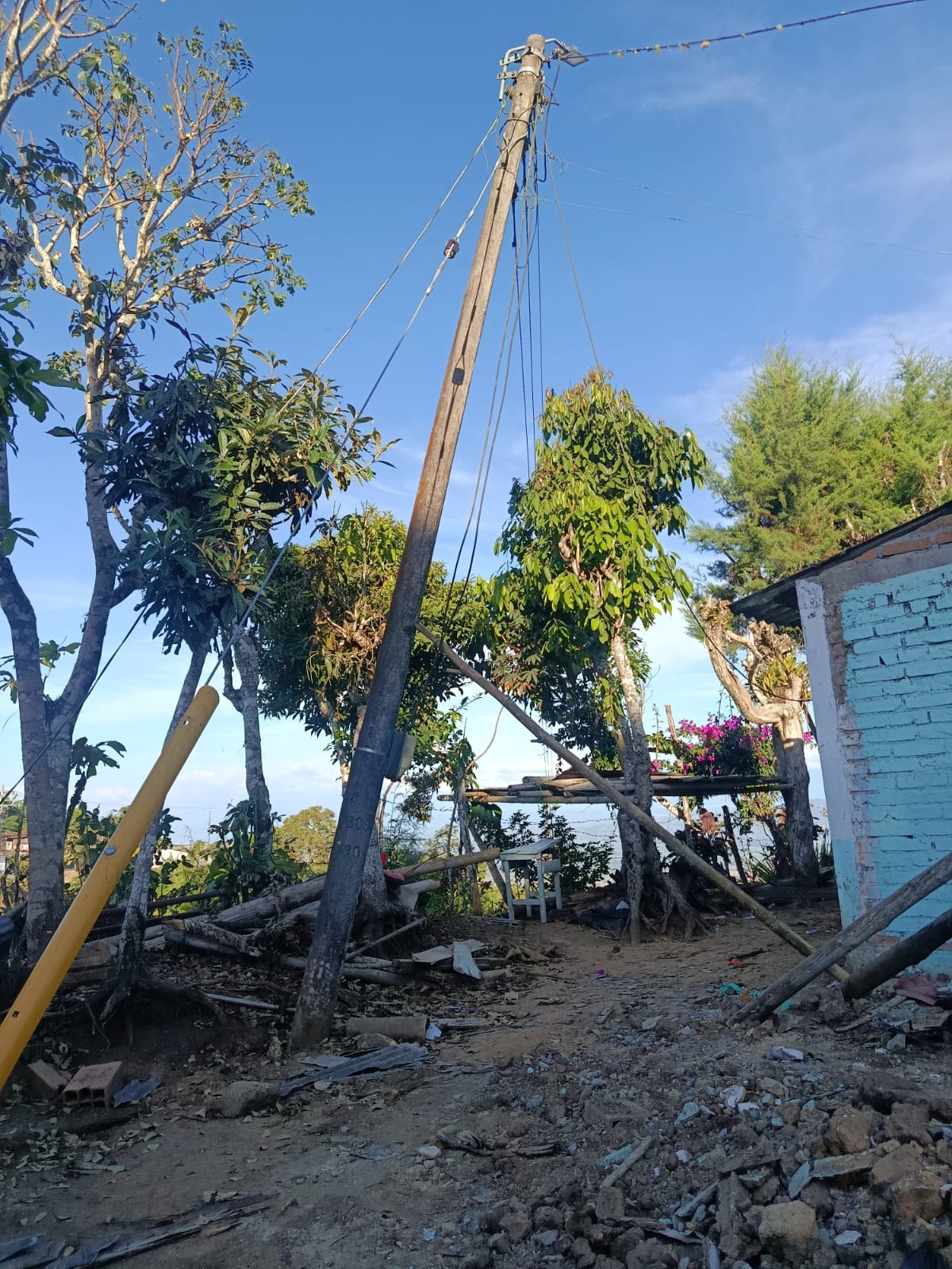 Poste de energía inclinado y sostenido con cables sobre un terreno con escombros
