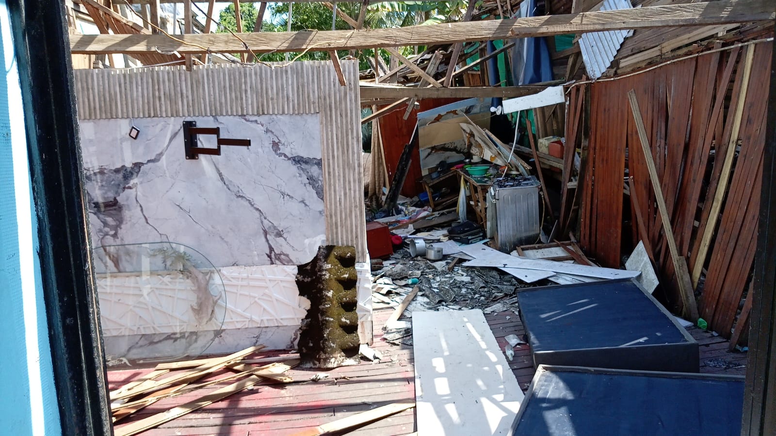 Interior de una vivienda de madera con el techo caído y los enseres entre los escombros