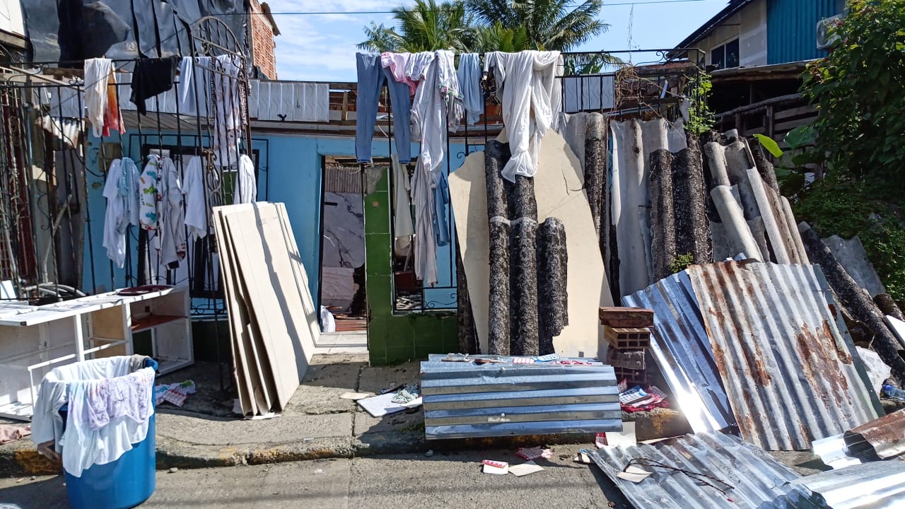 Ropa tendida y láminas de zinc apoyadas en la calle frente a las viviendas dañadas