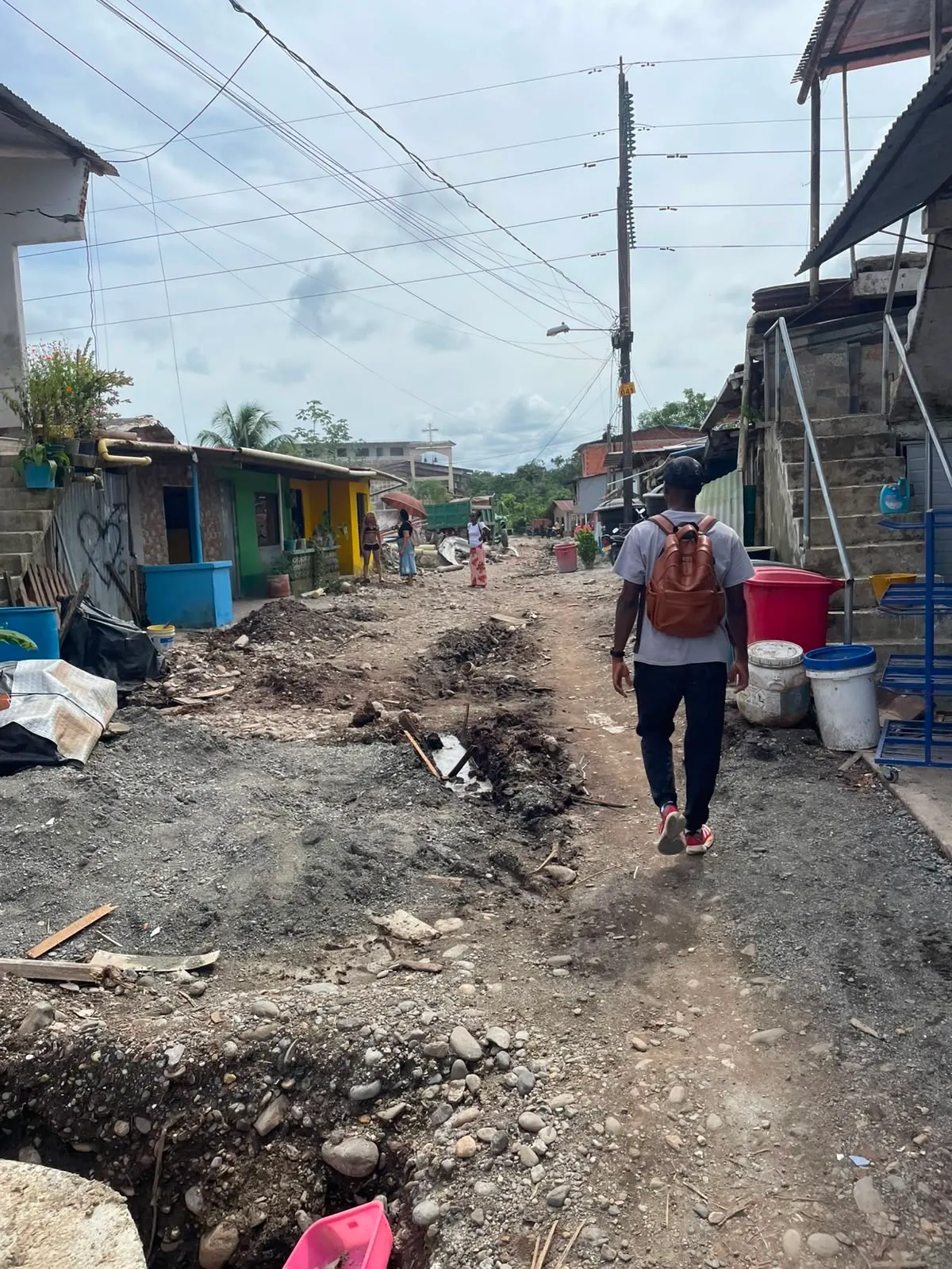 Persona caminando por una calle destapada de un pueblo, entre casas dañadas